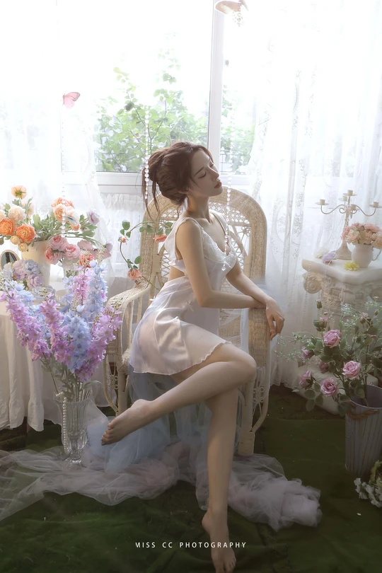 一个穿着白色连衣裙的年轻女子坐在花瓶前的椅子上