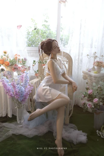 一个穿着白色连衣裙的年轻女子坐在花瓶前的椅子上