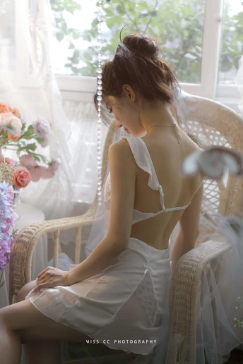 一个穿着白色连衣裙的年轻女子坐在窗前的一把椅子上