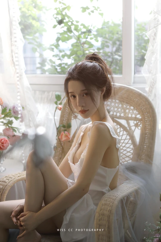 一个穿着白色连衣裙的年轻女子坐在靠近窗户的白椅子上