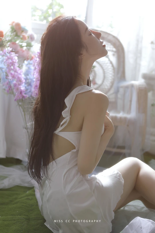 一个穿着白色连衣裙的年轻女子坐在床前窗前