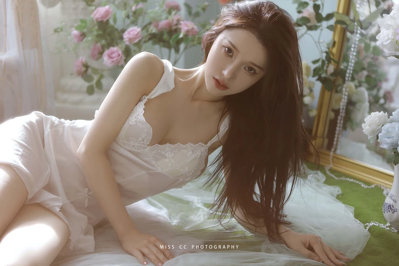 一个穿着白色连衣裙的年轻女子躺在床上 床边有一幅画。