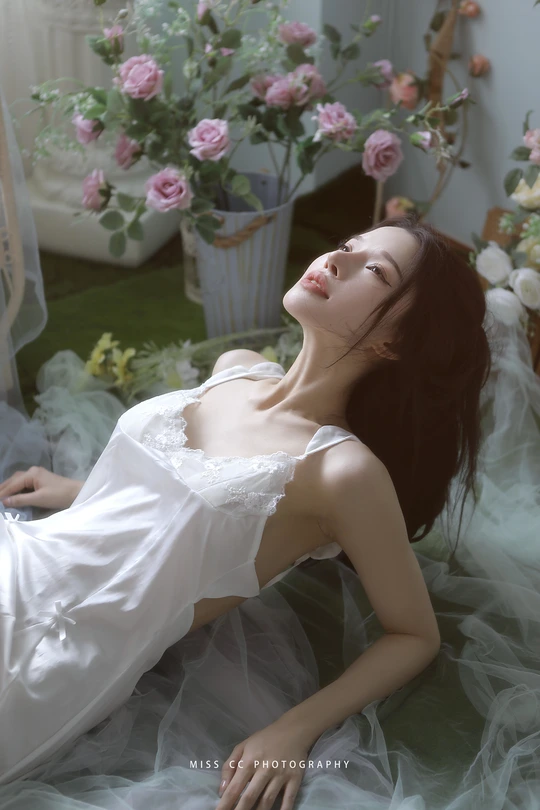 一个穿着白色连衣裙的年轻女士躺在地上 旁边有一台笔记本电脑和鲜花。