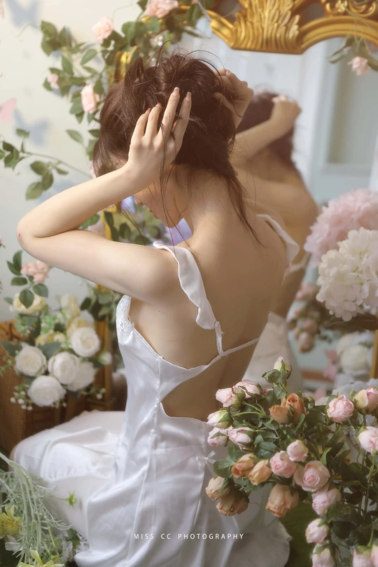 一位穿着白色连衣裙的年轻女子站在镜子前