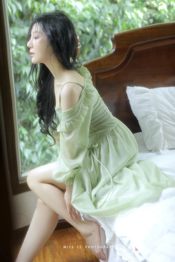 一个穿着绿色连衣裙的年轻女子坐在床上