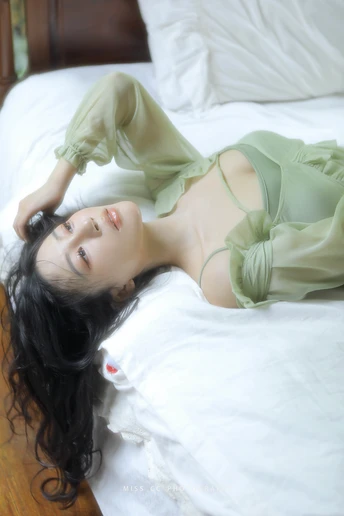 一个穿着绿色连衣裙的年轻女子躺在铺有白色床单的白色床上