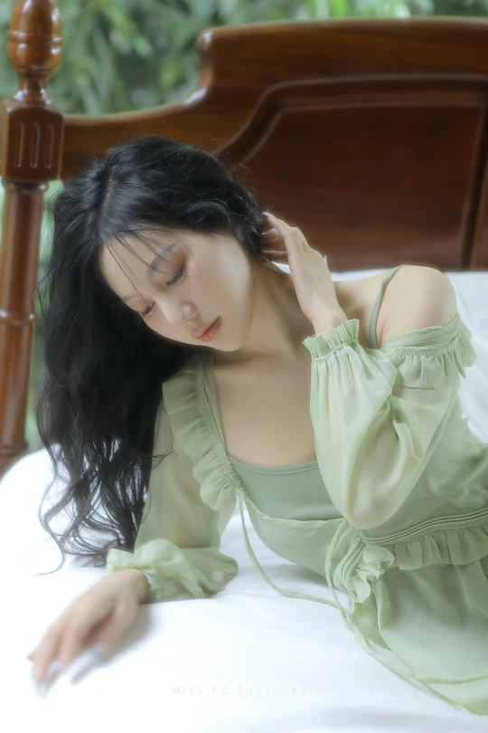 一个穿着绿色连衣裙的年轻女子躺在白色床上