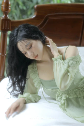 一个穿着绿色连衣裙的年轻女子躺在白色床上