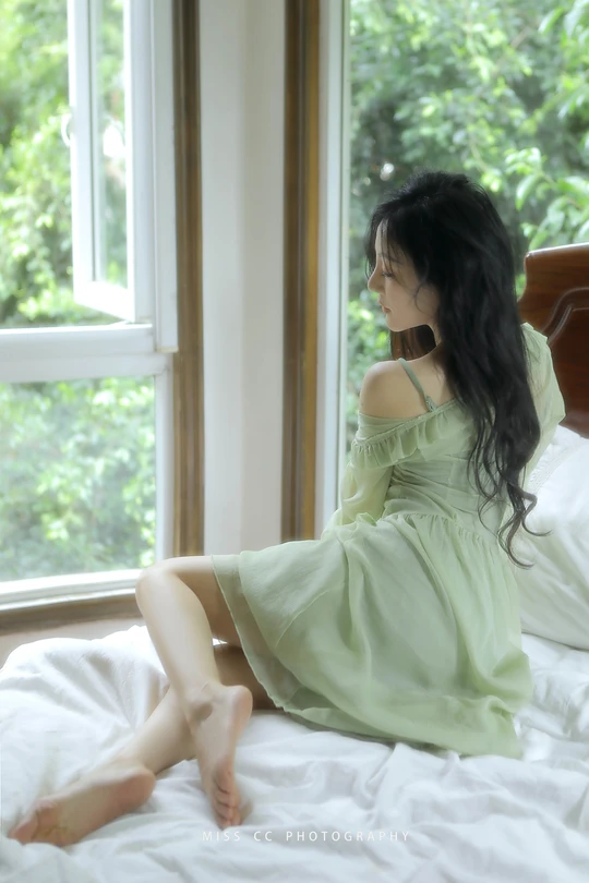 一个穿着绿色连衣裙的年轻女子坐在一张白色床上