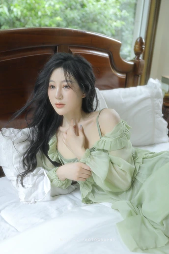 一个穿着绿色连衣裙的年轻女子坐在床上 头发凌乱地飘在空中。