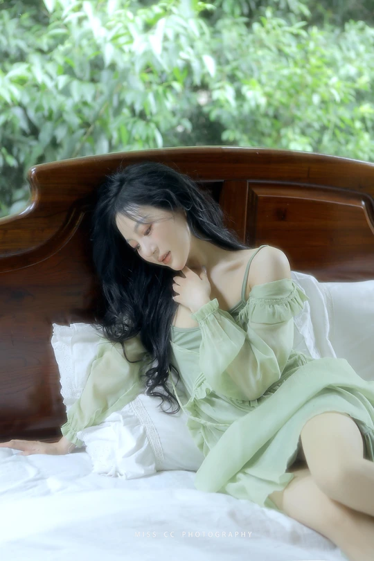 一个穿着绿裙子的年轻女子坐在床上 头发披散