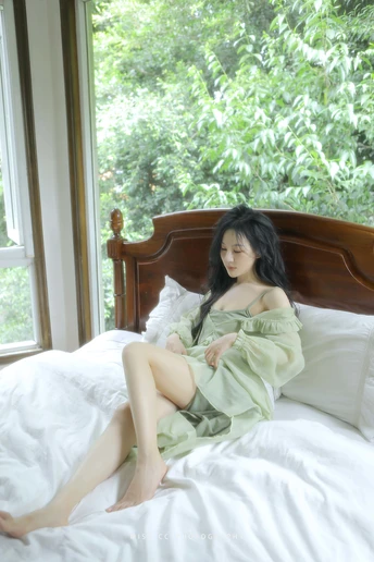 一个年轻女子坐在靠近窗户的白床上