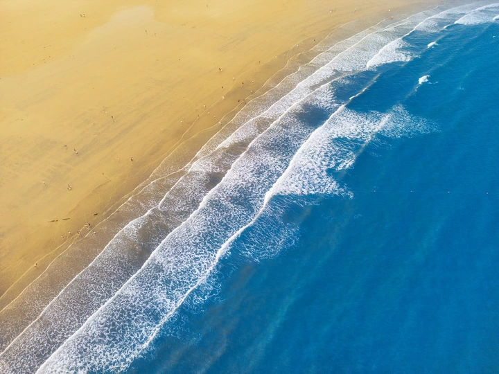 沙质海滩的 aerial view 带有蓝色水域和波浪。