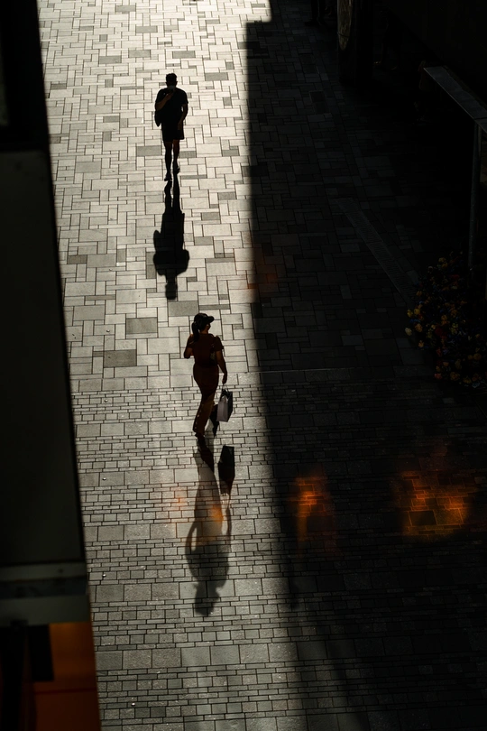 几个撑着雨伞的人走在一栋楼旁边的人行道上