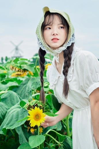 一个穿着连衣裙、戴着帽子的年轻女子站在向日葵地里 手里拿着一朵黄色的花