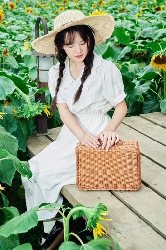 在美丽的向日葵地里 一个穿着连衣裙、戴着帽子的年轻女孩坐在长椅上 手里拿着一篮向日葵