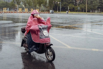 在雨中 一位穿着雨衣的女士骑着滑板车在停车场与其他骑摩托车的人一起驾驶。