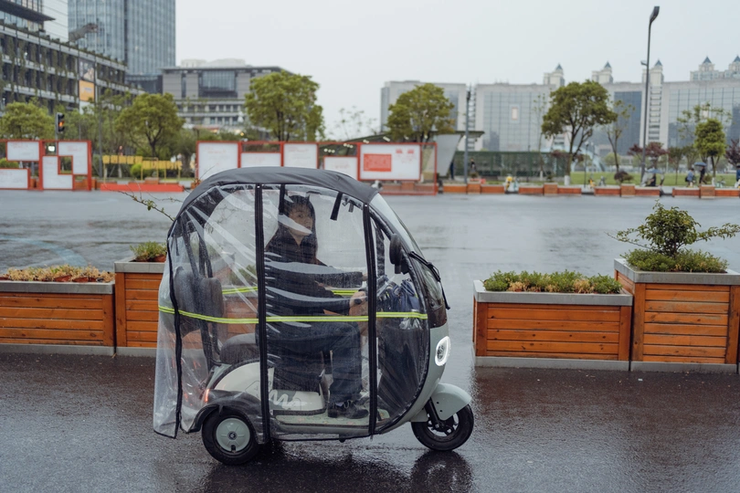 在雨中 一个驾驶小轮车的男人在街道上行驶。