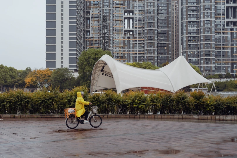 一个人穿着黄雨衣骑自行车在雨中 在大楼前。