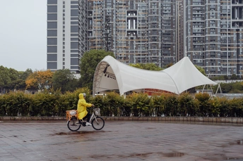 一个人穿着黄雨衣骑自行车在雨中 在大楼前。