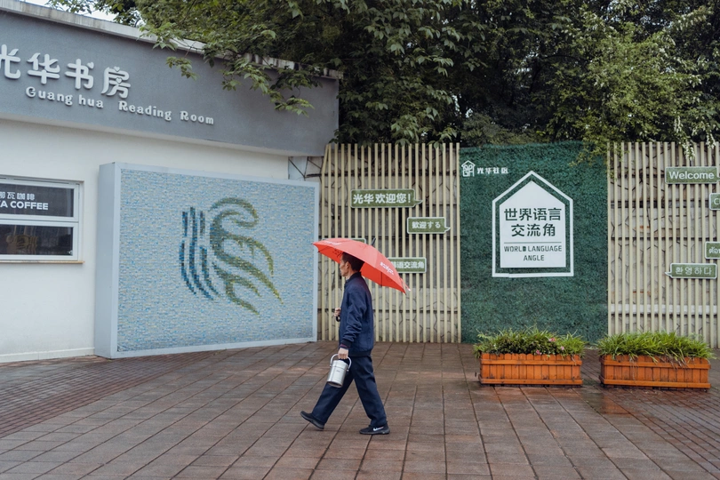 一位女士拿着红伞走在靠近建筑物的人行道上