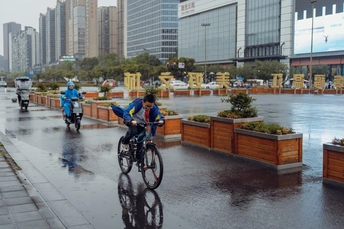 在一个城市的一个湿漉漉的街道上 人们骑着自行车 自行车手们带着伞在人行道上。