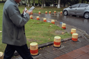 一个在雨中走人行道 地上有杯子 后面有辆车。