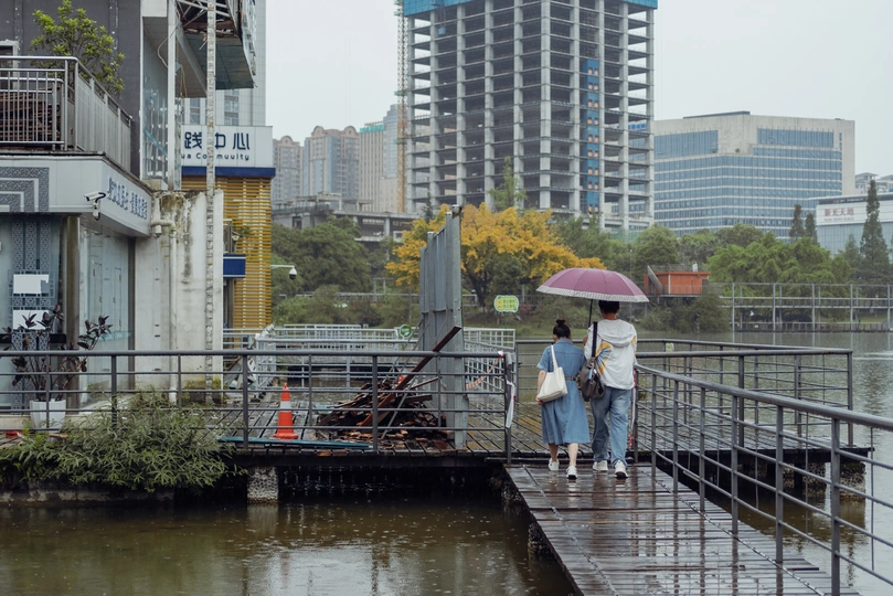 一些人拿着雨伞穿越一座跨越水域的城市桥梁 背景是建筑物。