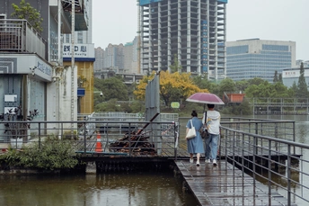 一些人拿着雨伞穿越一座跨越水域的城市桥梁 背景是建筑物。
