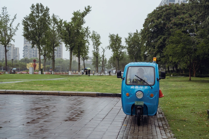 一个小蓝汽车在公园前面的湿人行道上行驶 摩托车停在街边。