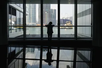 一位站在大型窗户前 凝视着水面上的城市倒影的女人剪影