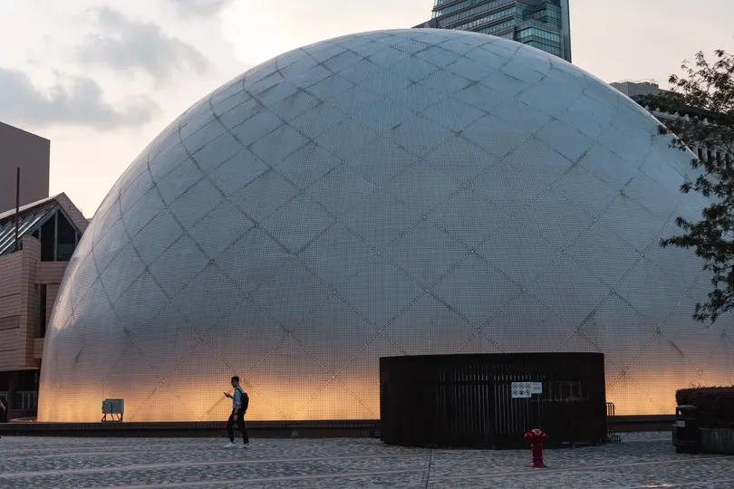 一个人站在城市中的一座大型白色圆顶建筑前 背景有其他建筑物。