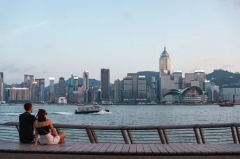 一位男性和一位女性坐在长凳上 眺望着水面 背景是城市天际线。