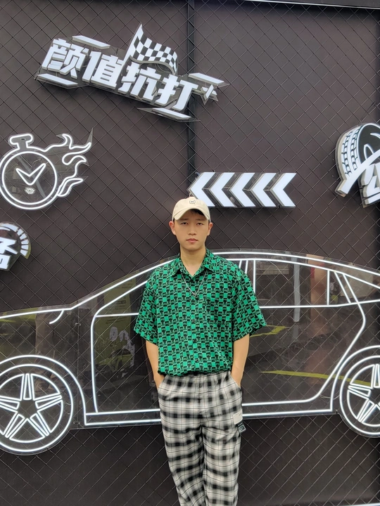 一名身穿绿色衬衫和格纹裤的年轻男子在汽车主题墙前摆姿势拍照