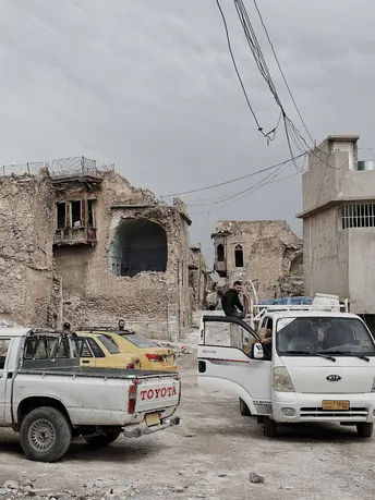 一辆白色卡车和其他停在城市的旧建筑废墟前面的车辆。