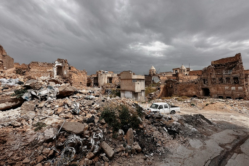 一辆白色的汽车停在古老的城镇废墟中 前景中有建筑和瓦砾。