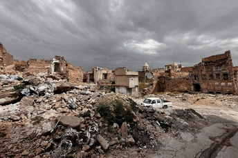 一辆白色的汽车停在古老的城镇废墟中 前景中有建筑和瓦砾。