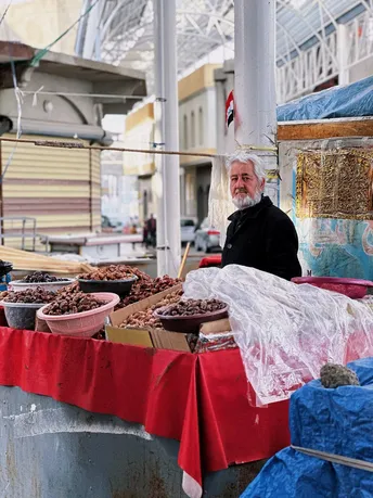 一个老人站在一张桌子前售卖食物。