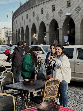 一些人站在一个户外咖啡馆外面 桌子上放着花。