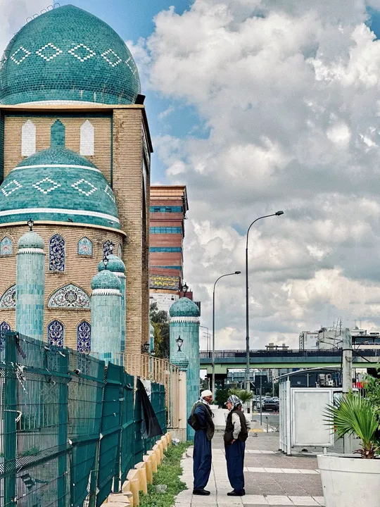 一些男人站在人行道上 旁边是绿色的围栏和蓝色的清真寺。