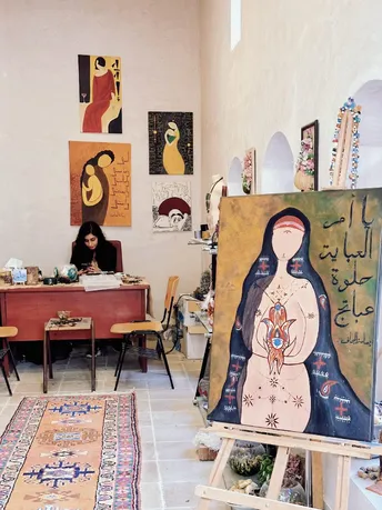 一个房间 一个艺术家坐在桌子前 桌子前面有一幅画 画中是一个女人 女人坐在地毯上。