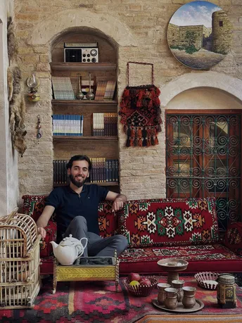 一个男子坐在带有地毯和其他家具的家庭房间里的沙发上。