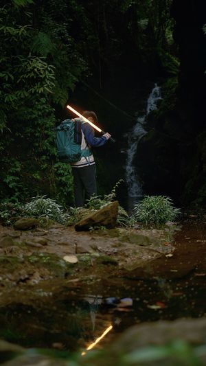 一个背着书包的男子站在夜晚的森林小溪旁 手里拿着手电筒。