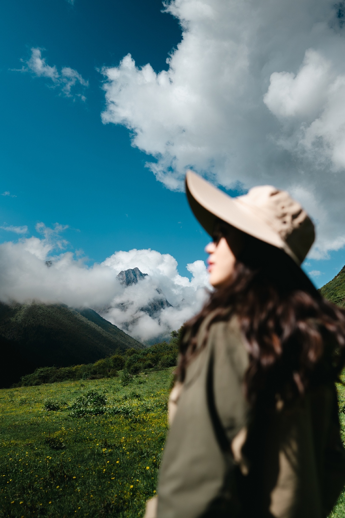 一位戴着牛仔帽的女人穿过一个绿意盎然的山谷 天空中飘着山和云。