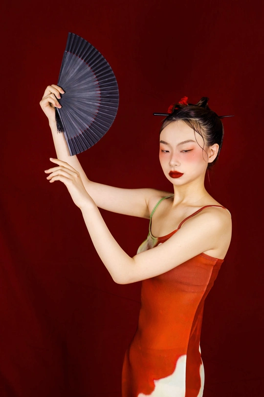 一位穿着红裙子的年轻女子手持扇子和雨伞