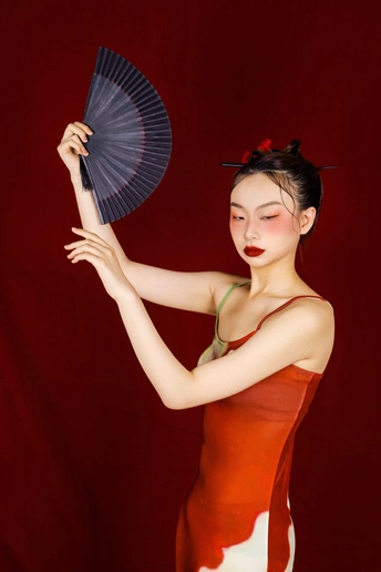 一位穿着红裙子的年轻女子手持扇子和雨伞