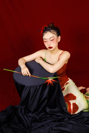 一个穿着黑色连衣裙 戴着红色帽子的女人坐在红色背景上。