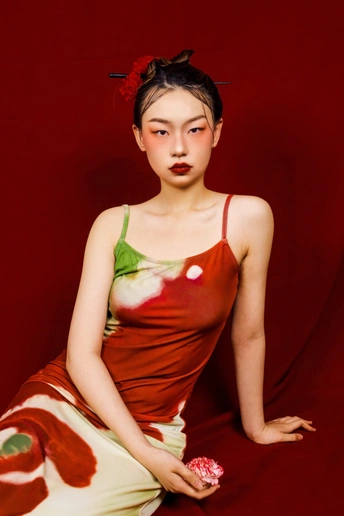 一位穿着红色连衣裙上带有花的年轻女子在红色背景上摆姿势