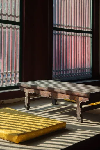 一个空房间 配有木床、长凳、地毯、枕头和一扇大窗户。