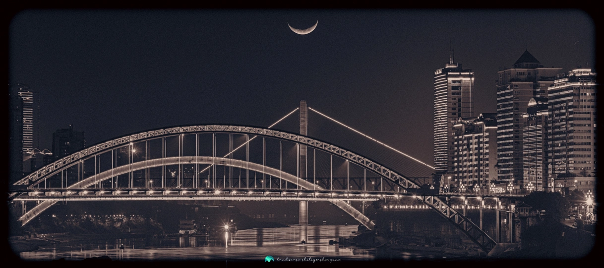 夜晚跨河大桥的照片 背景中有月亮和建筑物